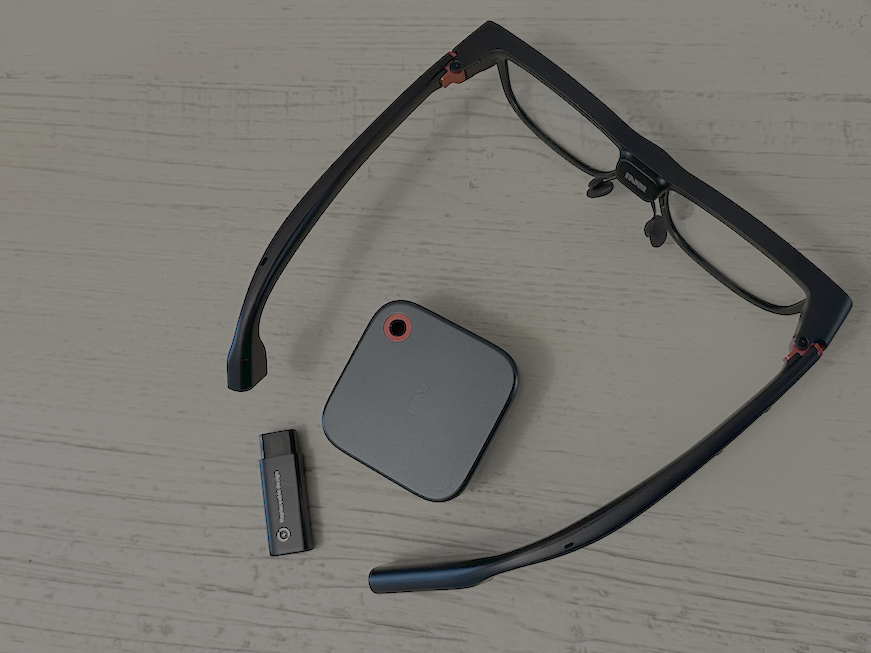 smart glasses lying on a table with rechargeable battery and charger